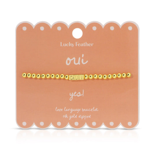 The image shows a gold-colored beaded bracelet with the word 'OUI' spelled out in letter beads, displayed on a peach-colored product card.