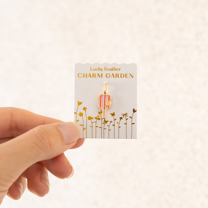 A hand holds a 'Lucky Feather Charm Garden' card with a pickleball paddle charm attached.