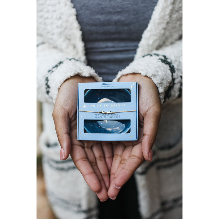 A person holding a light blue gift box set with the words 'SHINE SO BRIGHT' in their hands.