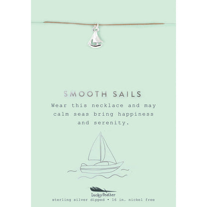 A silver sailboat charm necklace hangs on a card with a sailboat illustration and the phrase 'Smooth Sails.'