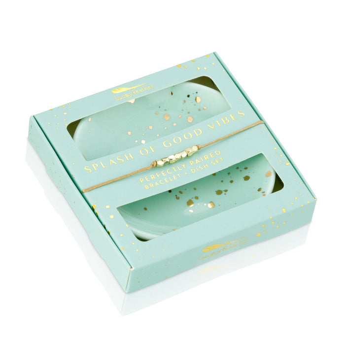 A gift box containing two teal dishes with gold accents and a beaded bracelet.