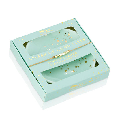 A gift box containing two teal dishes with gold accents and a beaded bracelet.