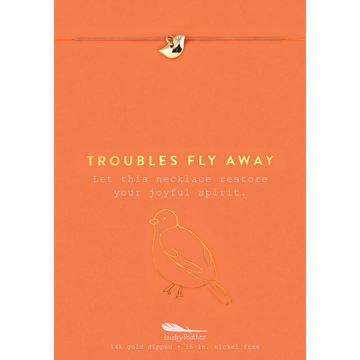 An orange card with a gold-colored bird charm, a gold-colored bird outline, and the words 'Troubles Fly Away.'
