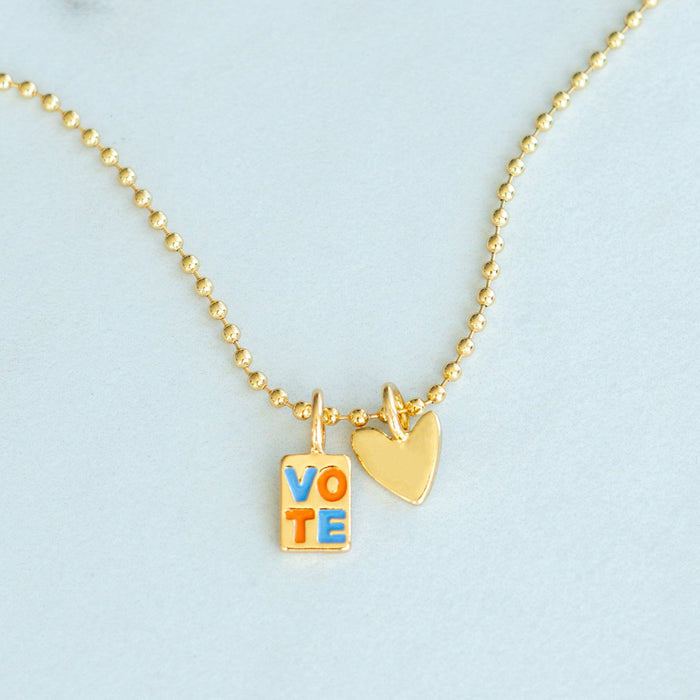 A gold ball chain necklace features 'VOTE' and heart charms.