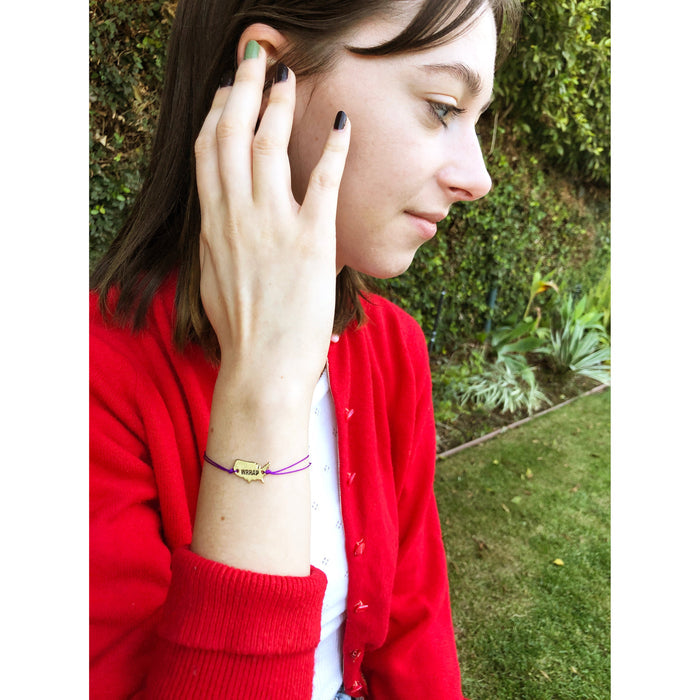 A person in a red cardigan looks to the side, with a purple bracelet featuring a 'WRRAP' charm visible on their wrist.