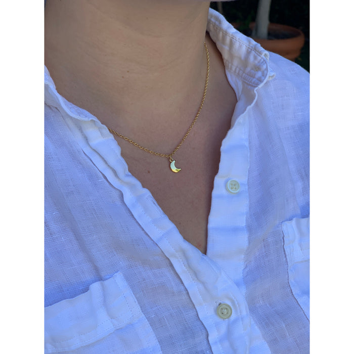 A person is wearing a white button-down shirt and a gold necklace with a small crescent moon pendant.