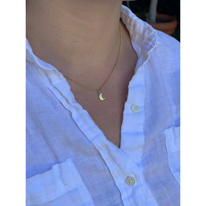 A person is wearing a white button-down shirt and a gold necklace with a small crescent moon pendant.