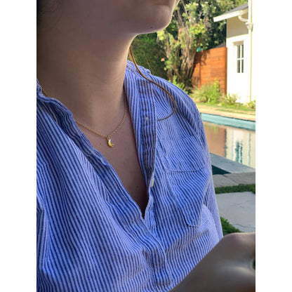 A person in a blue-and-white striped shirt wears a gold necklace with a crescent moon pendant.