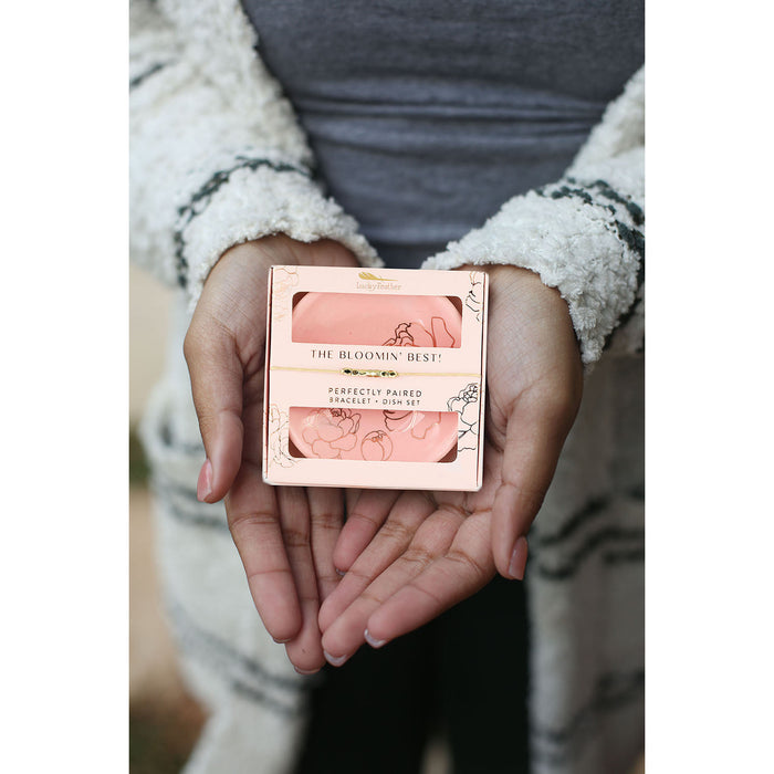 A person holds a 'Lucky Feather' gift set box for a bracelet and dish in their hands.